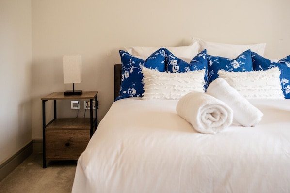 A hotel room with a bed, a nightstand, a lamp, and a rolled towel.