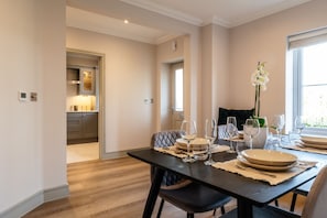 A dining area with a table set for four, a kitchen in the background, and a window with natural light.