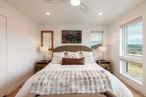 A bedroom with a large bed, two bedside tables, a ceiling fan, a painting, and a window with a view. - Deer Valley townhome with 4 bedrooms, hot tub, ski views. (Heber City)