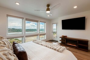 A modern bedroom with a large bed, a fireplace, a TV, and a balcony with a view of the landscape. - Deer Valley townhome with 4 bedrooms, hot tub, ski views. (Heber City)