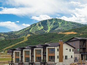 A modern multi-story building with large windows and a mountain backdrop. - Deer Valley townhome with 4 bedrooms, hot tub, ski views. (Heber City)