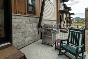 A patio with a grill, stone wall, and a view of the countryside. - Deer Valley townhome with 4 bedrooms, hot tub, ski views. (Heber City)