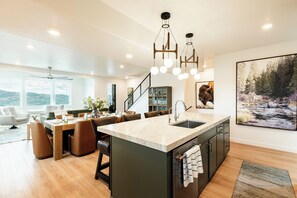 Une cuisine moderne dotée d’un îlot central, d’un coin repas avec des chaises et offrant une vue sur l’extérieur.