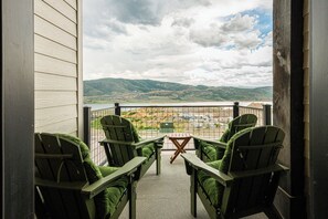 Un balcon avec quatre fauteuils Adirondack verts, une table en bois et une vue sur un lac et des collines.