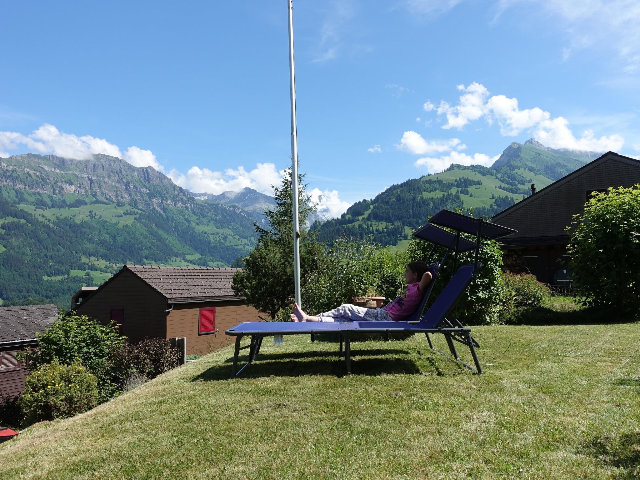 Une personne se détend sur un fauteuil bleu dans un espace verdoyant, avec une vue sur des montagnes en arrière-plan.