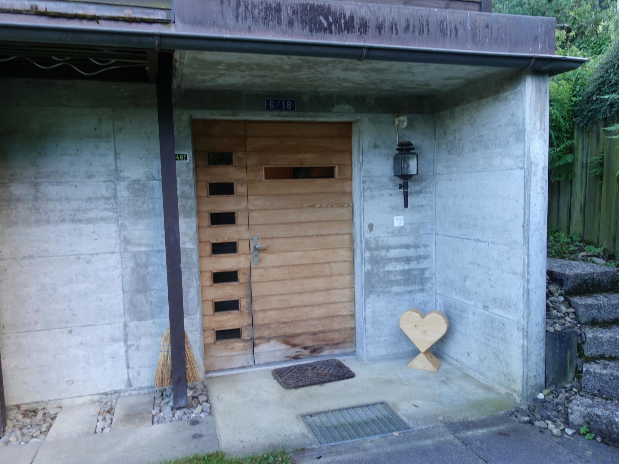 A concrete building entrance with a wooden door, a heart-shaped decoration, and a small window.