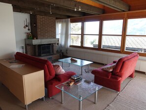 A living room with a fireplace, red sofas, a glass coffee table, and a view of the outdoors. - Bergperle Ferienhaus, Dusche, WC, Terrasse Ferienhaus, Dusche, WC, Terrasse by Interhome (Frutigen)