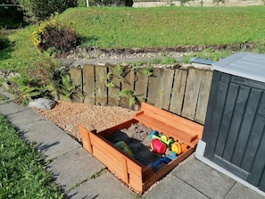 Ein erhöhter Blumenkasten mit Spielzeug und einem Gartenhaus im Hintergrund.