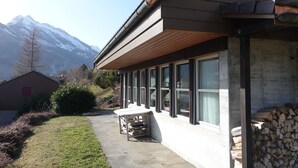 A building with a wooden roof and large windows, a concrete pathway, and a mountain backdrop.