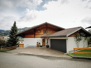 A wooden house with a garage, a paved driveway, and a mountain backdrop. - Alba Appartement/Fewo, Dusche und Bad, WC, 1 Schlafraum 2.5-Zimmerwohnung by Interhome (Frutigen)