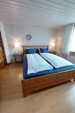 A double bed with a wooden frame, two bedside tables with lamps, and a wall-mounted decoration. - Chalet Edelweiss Appartement/Fewo, Dusche, WC, 2 Schlafräume 3-Zimmerwohnung by Interhome (Frutigen)