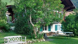 A rustic chalet with a wooden deck, a bench, and a dining table in a lush green setting. - Chalet Edelweiss Appartement/Fewo, Dusche, WC, 2 Schlafräume 3-Zimmerwohnung by Interhome (Frutigen)