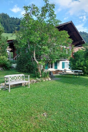 A rustic chalet with a wooden deck, a bench, and a dining table in a lush green setting. - Chalet Edelweiss Appartement/Fewo, Dusche, WC, 2 Schlafräume 3-Zimmerwohnung by Interhome (Frutigen)