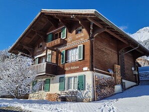 A wooden chalet with a balcony, a sign reading 'Da Liebe Gott macht schöne Dinge,' and a mountain backdrop. - Chalet Edelweiss Appartement/Fewo, Dusche, WC, 2 Schlafräume 3-Zimmerwohnung by Interhome (Frutigen)