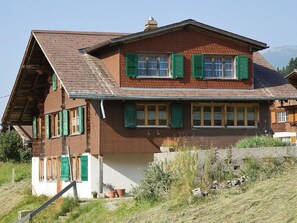 A two-story house with a sloped roof, green shutters, and a stone foundation. - Gehret Appartement/Fewo, Dusche, WC, 1 Schlafraum 2-Zimmerwohnung by Interhome (Adelboden)