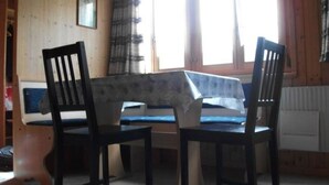 A room with a wooden interior, a table with a blue tablecloth, two chairs, a window with curtains, and a radiator. - Gehret Appartement/Fewo, Dusche, WC, 1 Schlafraum 2-Zimmerwohnung by Interhome (Adelboden)