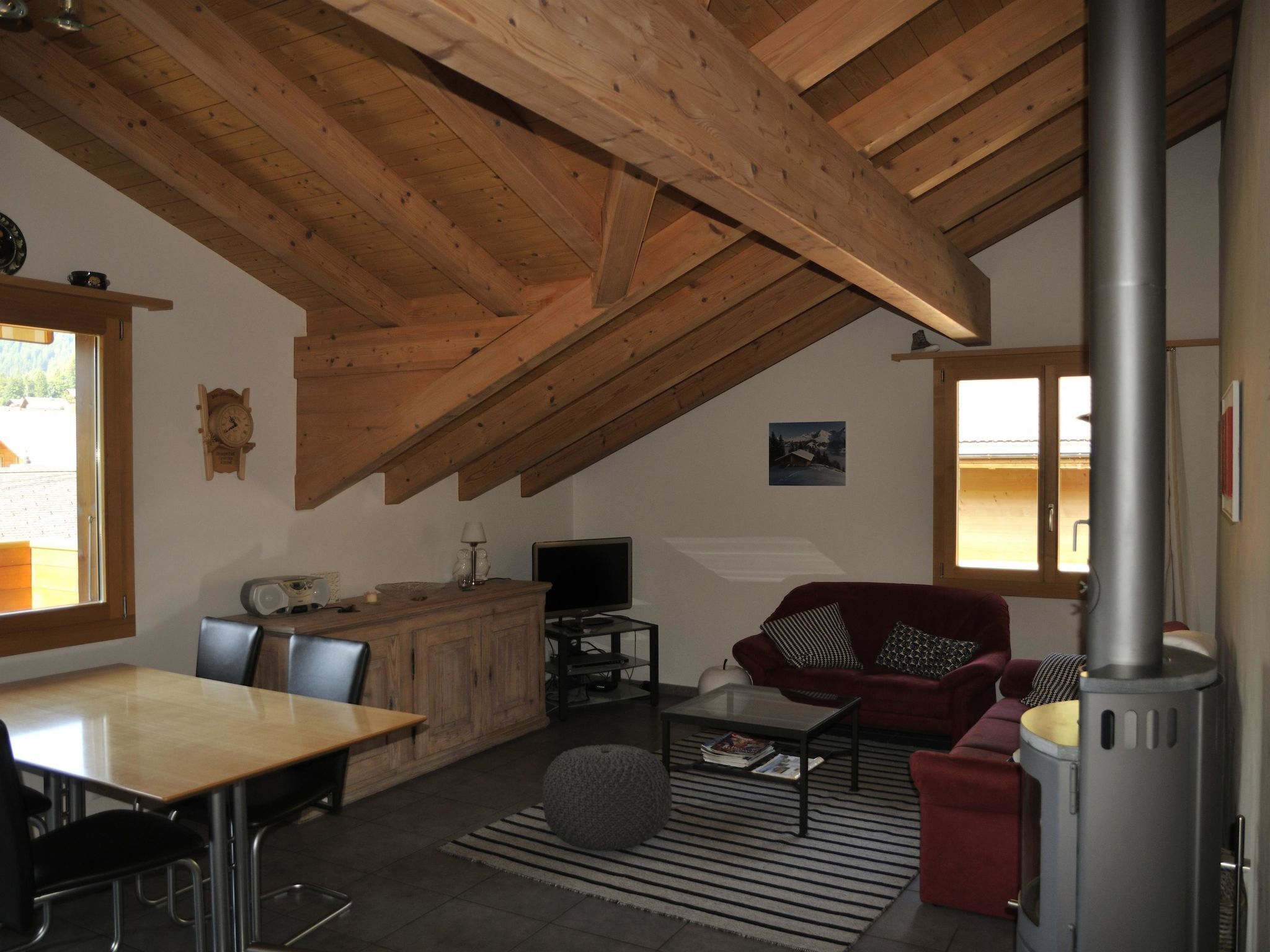 Un salon chaleureux avec un plafond en bois, une cheminée, un canapé, un téléviseur et un coin repas comprenant des chaises et une table.