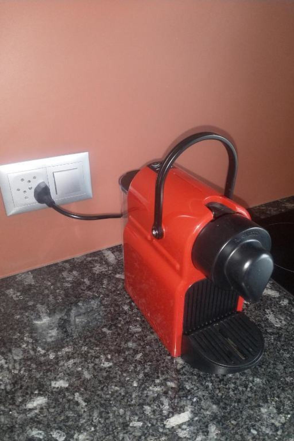 Un electrodoméstico rojo con un asa negra, conectado a un enchufe.