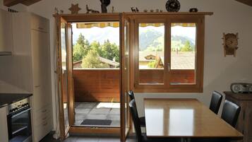 Une cuisine avec une porte ouverte donnant sur un balcon d’où l’on peut admirer la vue sur les montagnes.