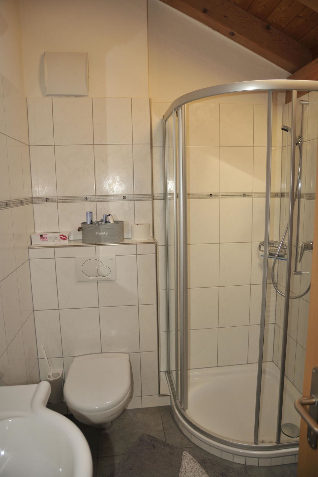 A bathroom with a shower, two toilets, and a washbasin.