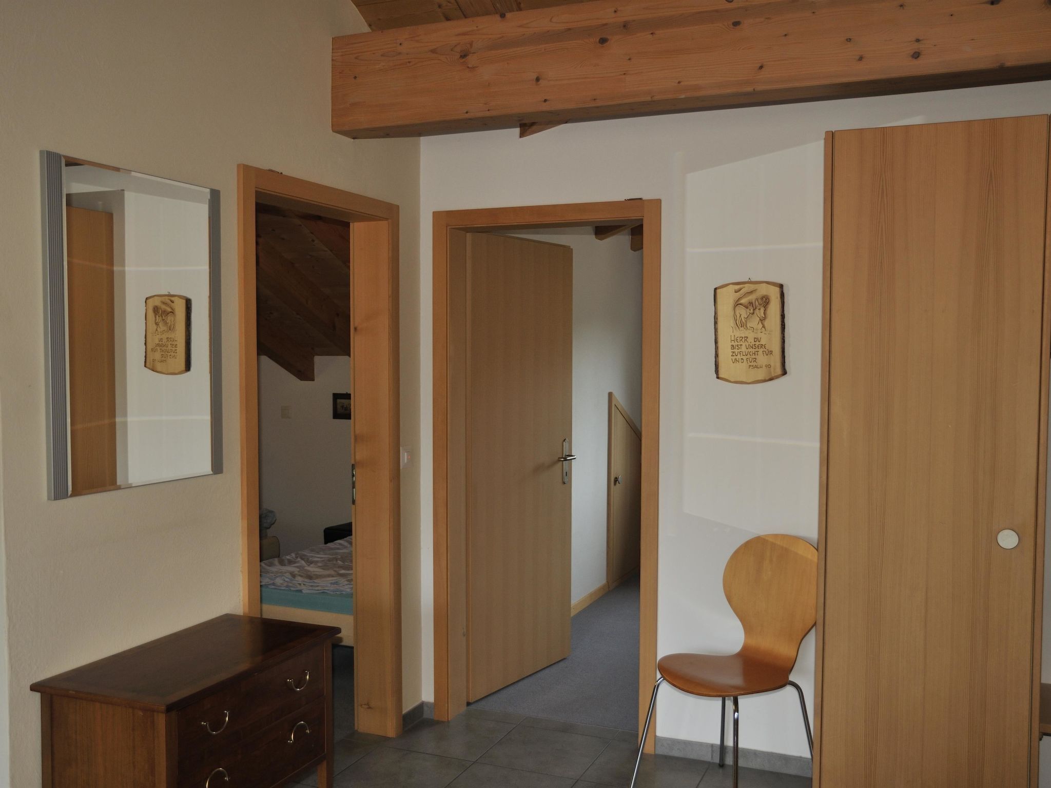 A room with a wooden dresser, a chair, and a door leading to another room.