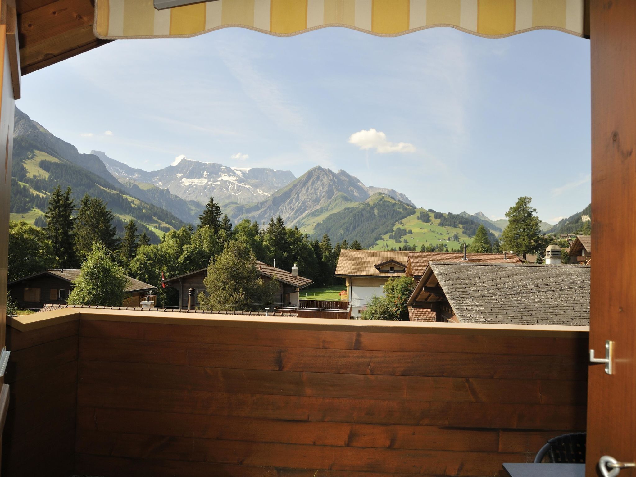 Un balcon en bois donnant sur un village, avec des maisons et des montagnes en arrière-plan.