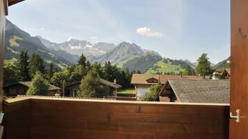 Un balcon en bois donnant sur un village, avec des maisons et des montagnes en arrière-plan.