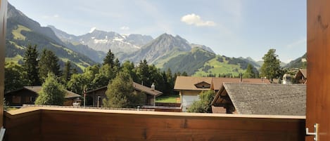 Een houten balkon met uitzicht op een dorp met huizen en bergen op de achtergrond.