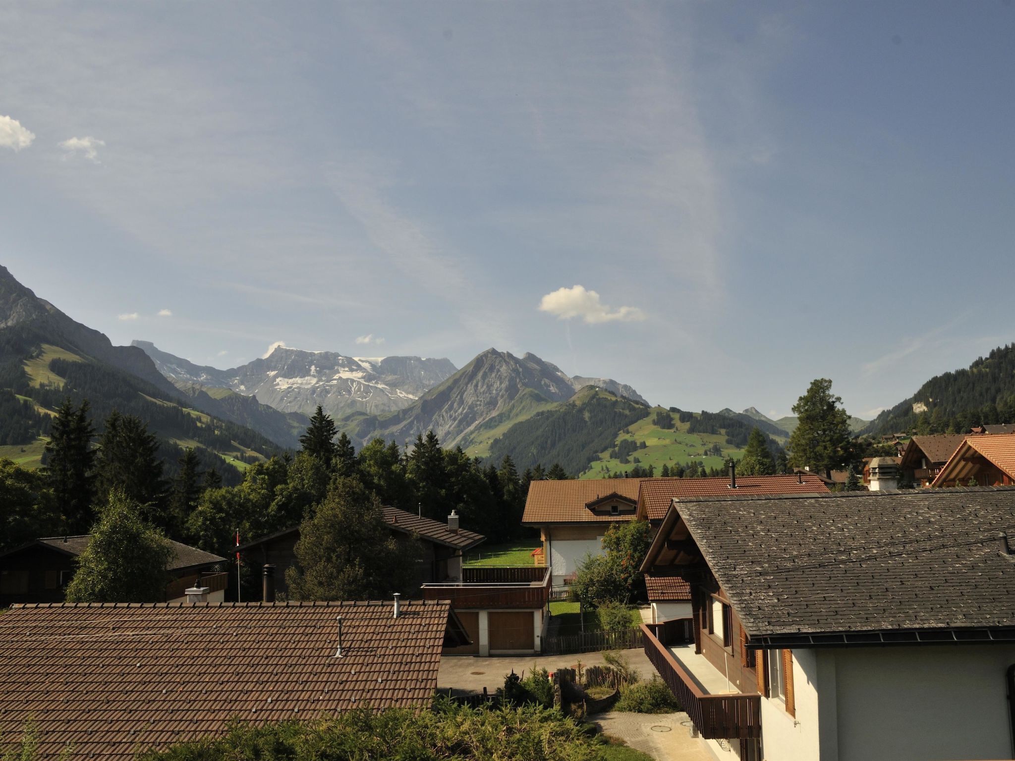 A mountain village with traditional houses, a clear sky, and snow-capped peaks in the background.