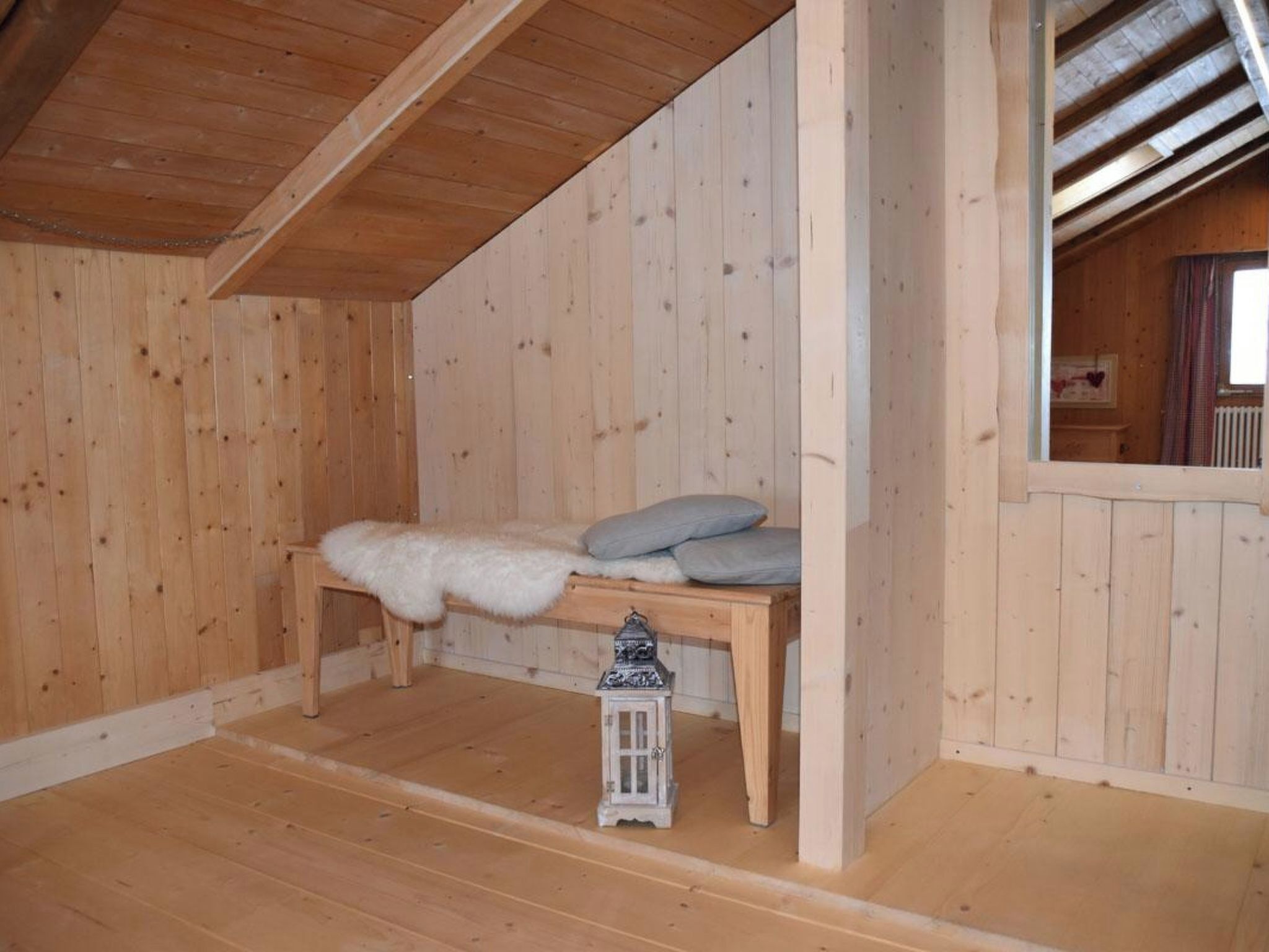 Une pièce en bois avec un banc, des coussins, une lanterne et une fenêtre.