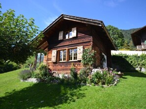 A wooden chalet with a sloped roof, large windows, and a well-maintained garden with various plants and flowers. - Gästehaus Alpengruss Ferienhaus, Dusche, WC, 1 Schlafraum Chalet by Interhome (Adelboden)