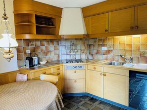 A compact kitchen with wooden cabinets, a gas stove, a sink, and a dining area with a table and chairs. - Juwel 2 Appartement/Fewo, Bad, WC, 2 Schlafräume 3.5-Zimmerwohnung by Interhome (Adelboden)