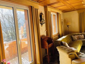 A room with a sofa, a wooden desk, a wall clock, and large windows with curtains. - Juwel 2 Appartement/Fewo, Bad, WC, 2 Schlafräume 3.5-Zimmerwohnung by Interhome (Adelboden)