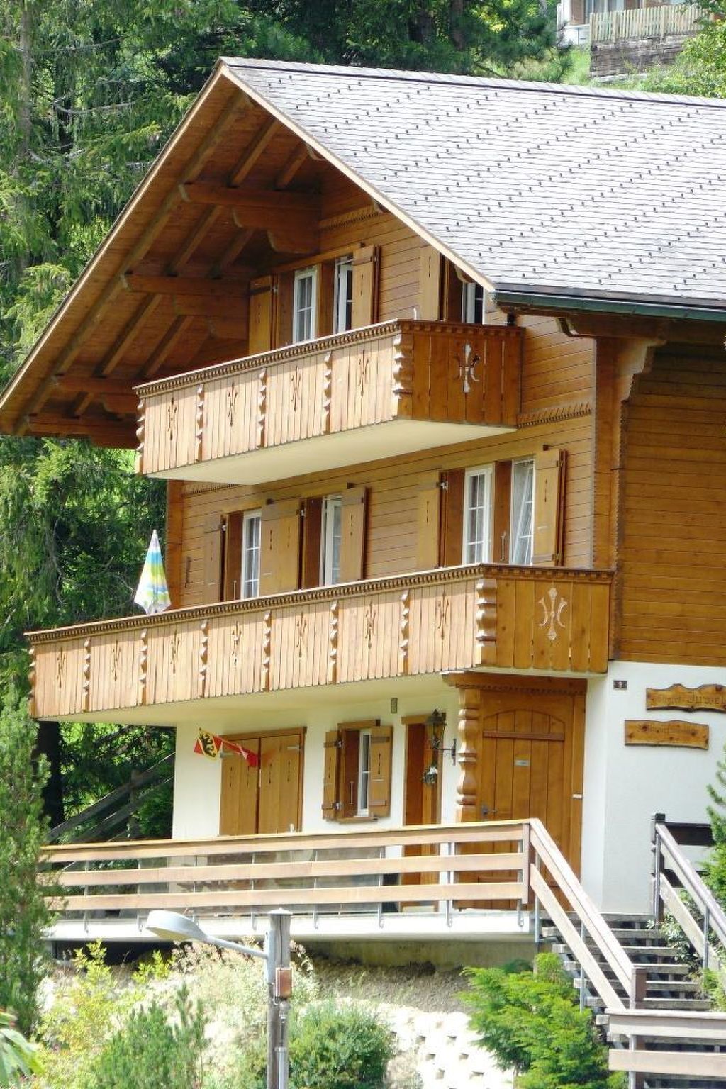 Eine mehrstöckige Holzhütte mit Balkonen, einer Treppe und Blick auf die umliegende Grünfläche.