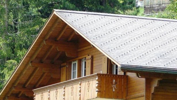 Un chalet in legno a più piani con balconi, una scala e vista sul verde circostante.