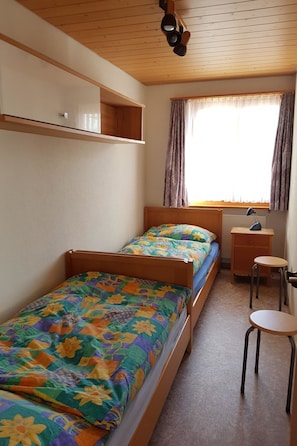 A small, single-bed room with a wooden ceiling, a window with curtains, a bedside table, and a chair. - Walt-Elis Appartement/Fewo, Bad, WC, 2 Schlafräume 3-Zimmerwohnung by Interhome (Adelboden)