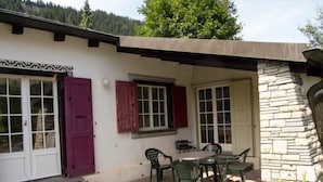 Edificio de fachada de piedra, con patio, mesa y sillas, y una puerta con ventana.