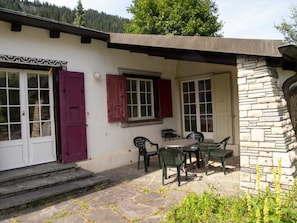 A building with a stone facade, a patio with a table and chairs, and a door with a window. - Baslerdybli Appartement/Fewo, Bad, WC, 3 Schlafräume 4-Zimmerwohnung by Interhome (Adelboden)