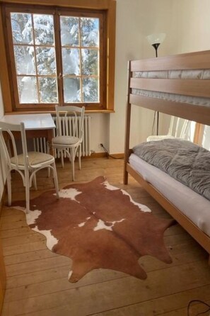 A room with a bunk bed, a desk with a chair, a cowhide rug, and a window with a view of trees. - Baslerdybli Appartement/Fewo, Bad, WC, 3 Schlafräume 4-Zimmerwohnung by Interhome (Adelboden)