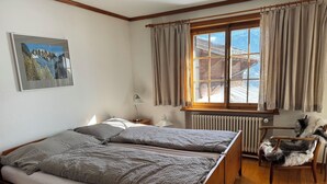 Un dormitorio con una cama de madera, una ventana con cortinas, un radiador, una silla y un tapete de piel de vaca.