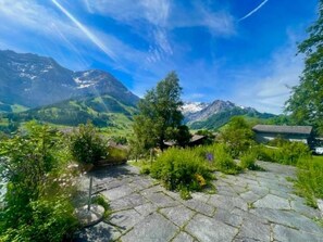 Ein Steinweg führt zu einem Blick auf das Gebirge, der Himmel ist wolkenlos.