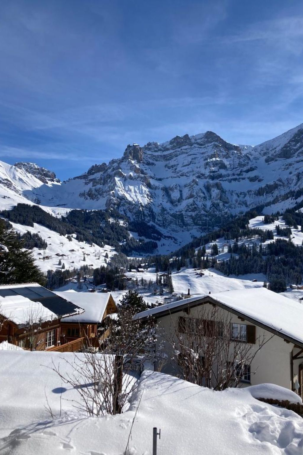 Paisaje montañoso nevado con una cabaña de madera y un edificio de techo inclinado.