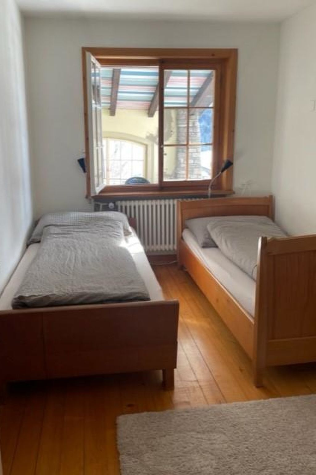 Une petite pièce avec deux lits en bois, un radiateur et une fenêtre donnant sur l’extérieur.