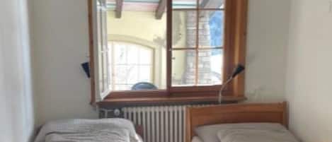 A small room with two wooden beds, a radiator, and a window with a view of the outside.