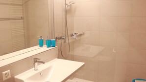 Ein Badezimmer mit weißem Waschbecken, einem Spiegel, einer Dusche und einem Handtuchhalter.