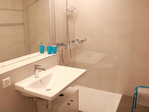 A bathroom with a white sink, a mirror, a shower, and a towel rack. - Rapunzel AP D22 Appartement/Fewo, Bad, WC, 2 Schlafräume 3-Zimmerwohnung by Interhome (Adelboden)