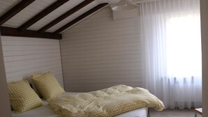 Ein Schlafzimmer mit einem Bett, Kissen, einem Fenster mit Vorhängen und einem Deckenventilator.