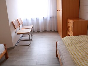 Ein Schlafzimmer mit einem Bett, einem Sessel, einem Kleiderschrank und einem Fenster mit Vorhängen.