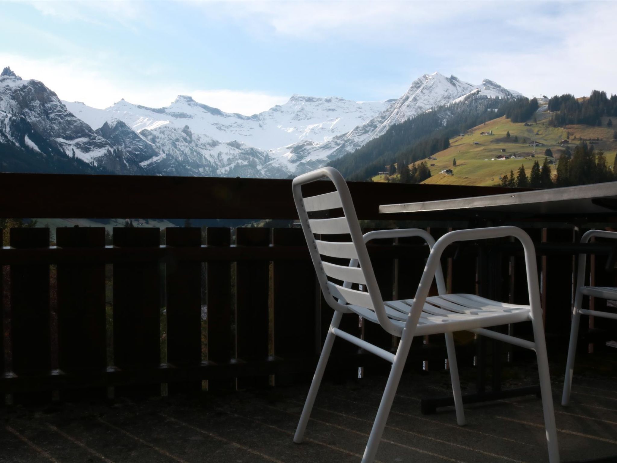 Un balcon avec une chaise et une table blanches donnant sur un paysage montagneux.