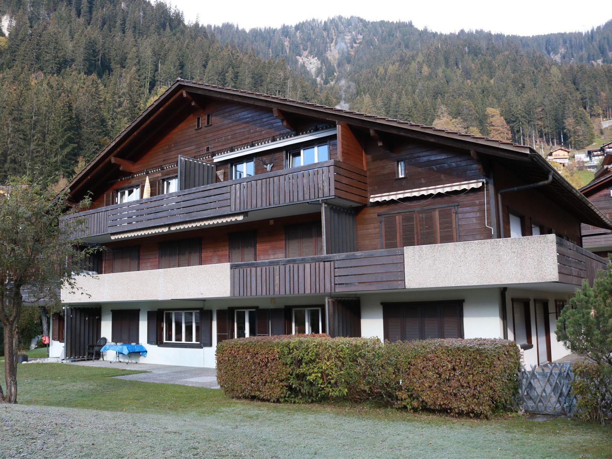 A multi-story wooden chalet with balconies, a covered porch, and a view of a forested mountain.